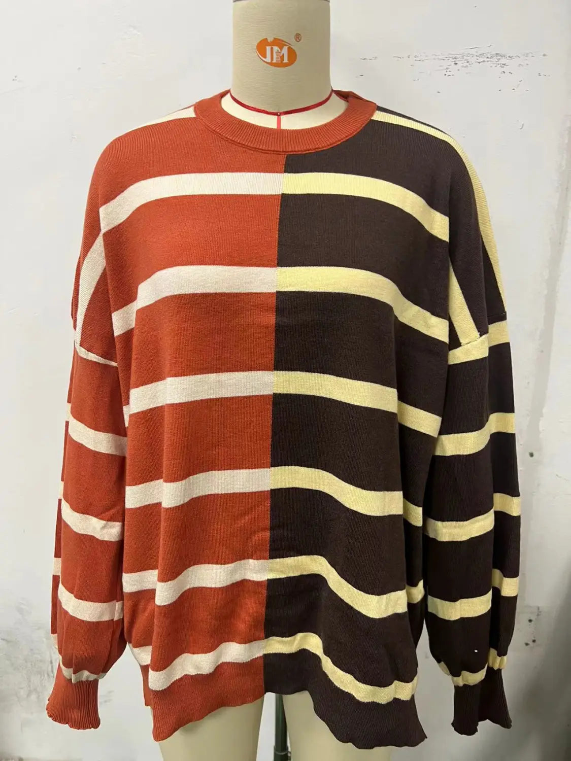 Woman’s oversized split color knit sweater with bold rust orange and deep brown halves and cream horizontal stripes made of cozy knit material