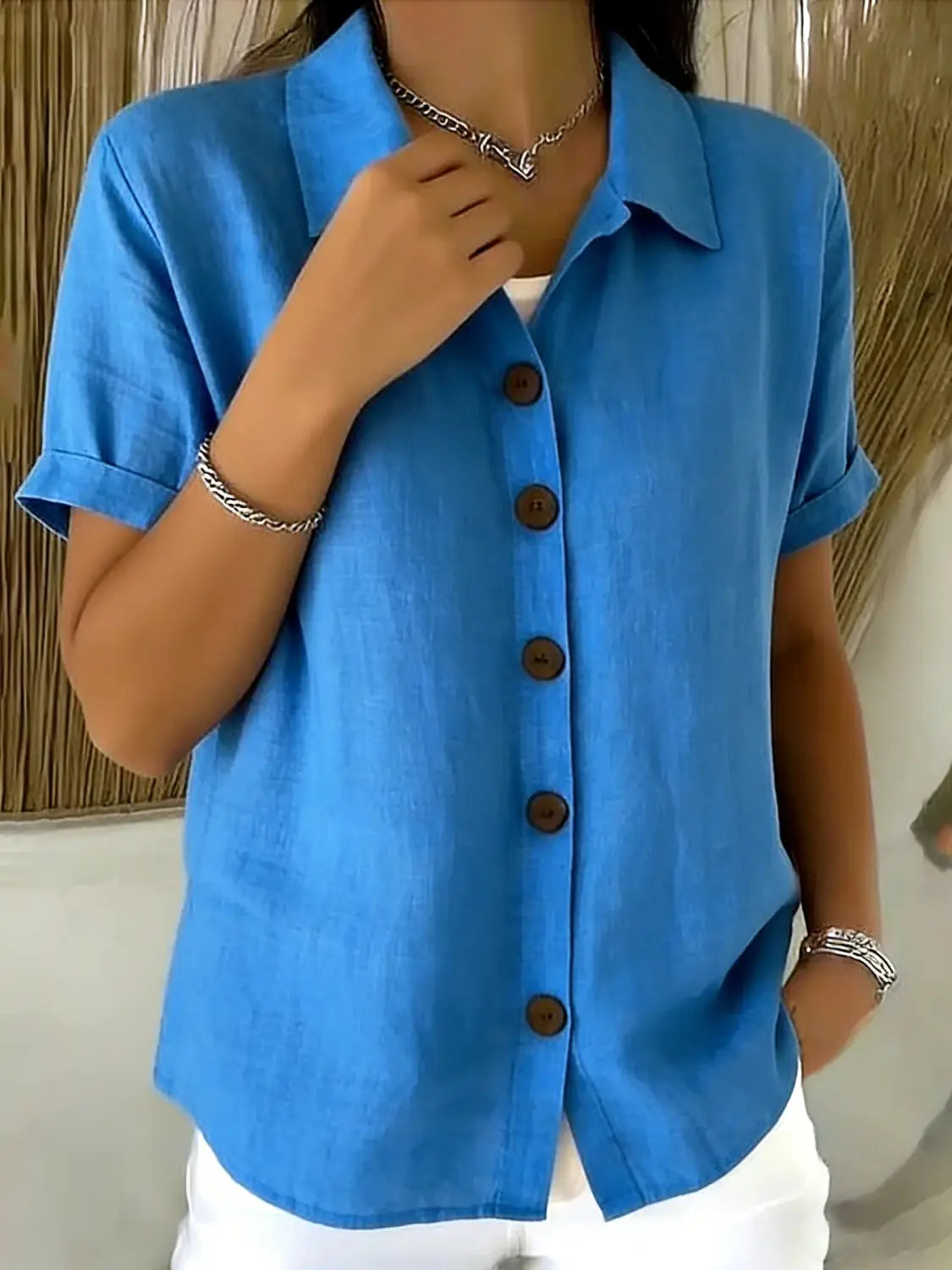 Camisa de manga corta de lino para mujer en azul brillante con cuello y botones de madera marrón, con puños enrollados.