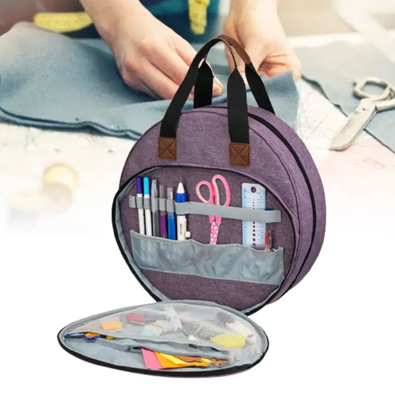 Premium circular embroidery and craft tool storage tote in purple with black handles and brown leather-like accents featuring organized compartments holding pens scissors rulers and craft supplies.