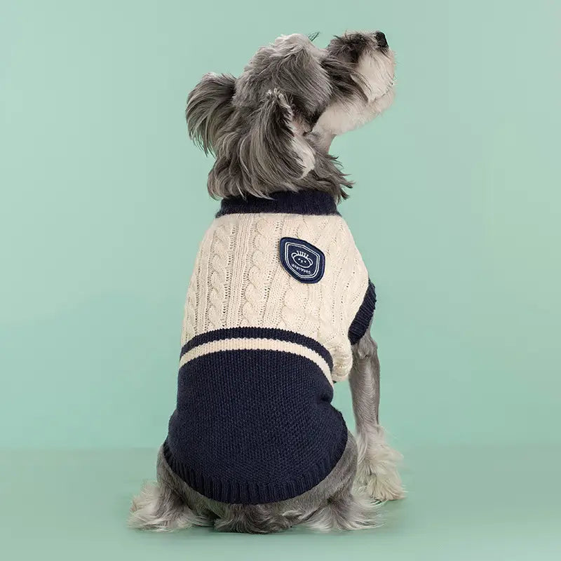 Creme- und navyblauer Zopfmuster-Hundepullover aus Strickmaterial mit kleinem besticktem Aufnäher auf der Rückseite, entworfen als warme Schuluniform-Tierbekleidung, von der Rückseite dargestellt.