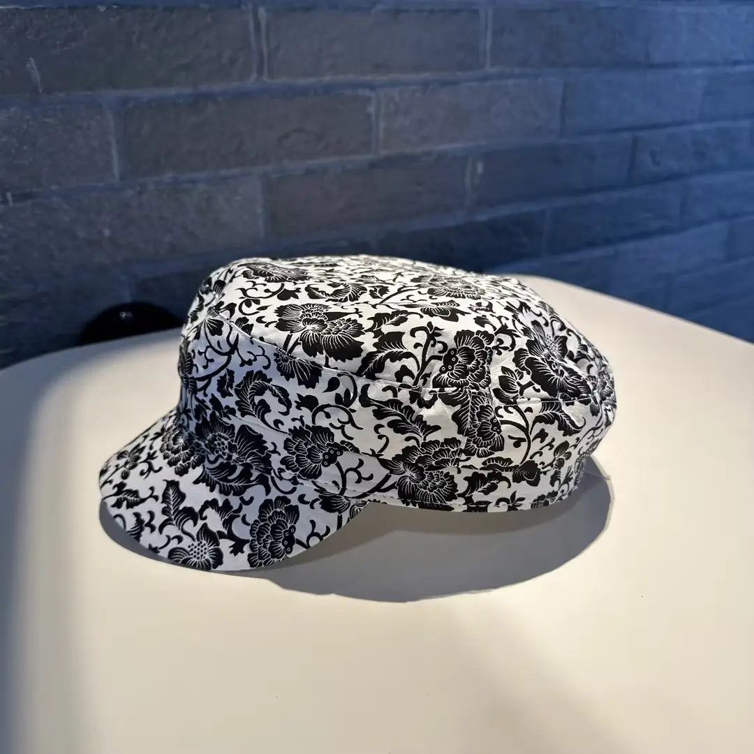 Gorra tipo bucket hat blanca de tela con un patrón floral negro marcado en diseño impreso estilo coreano.