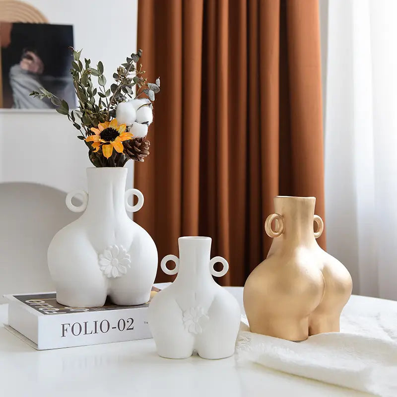 White ceramic female body vase shaped like buttocks with two circular handles and a raised floral design on the front.
