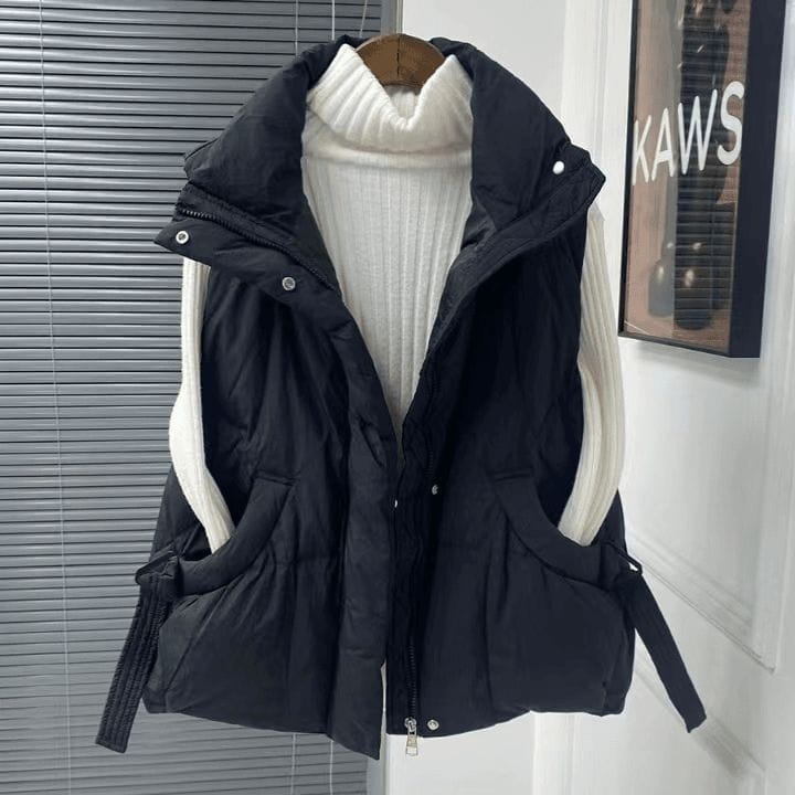 Schwarze Damen-gesteppten Pufferweste in großen Größen mit weißen gerippten Strickärmeln und Fronttaschen, hängend auf einem Holzkleiderbügel als Oberbekleidung in großen Größen.