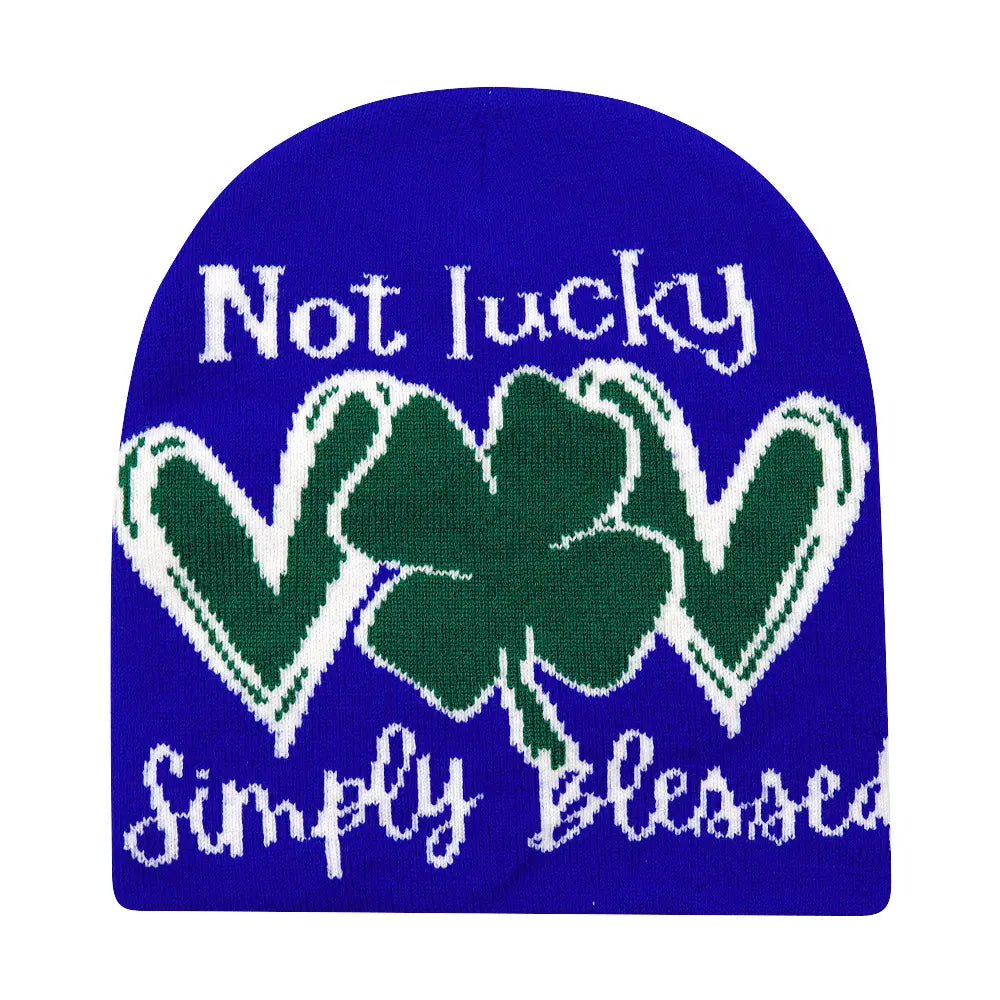 A vibrant royal blue knitted beanie made of warm fabric features a bold green shamrock with white outlining and the phrases not lucky above and simply blessed below in white knit lettering, ideal for winter wear.