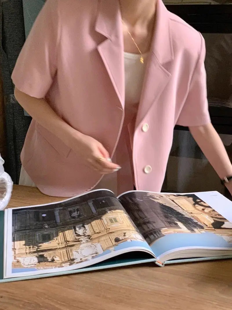 Un blazer pour femmes à manches courtes rose pâle, doté d’un col classique, de boutons blancs et d’une coupe décontractée adaptée à une tenue décontractée.