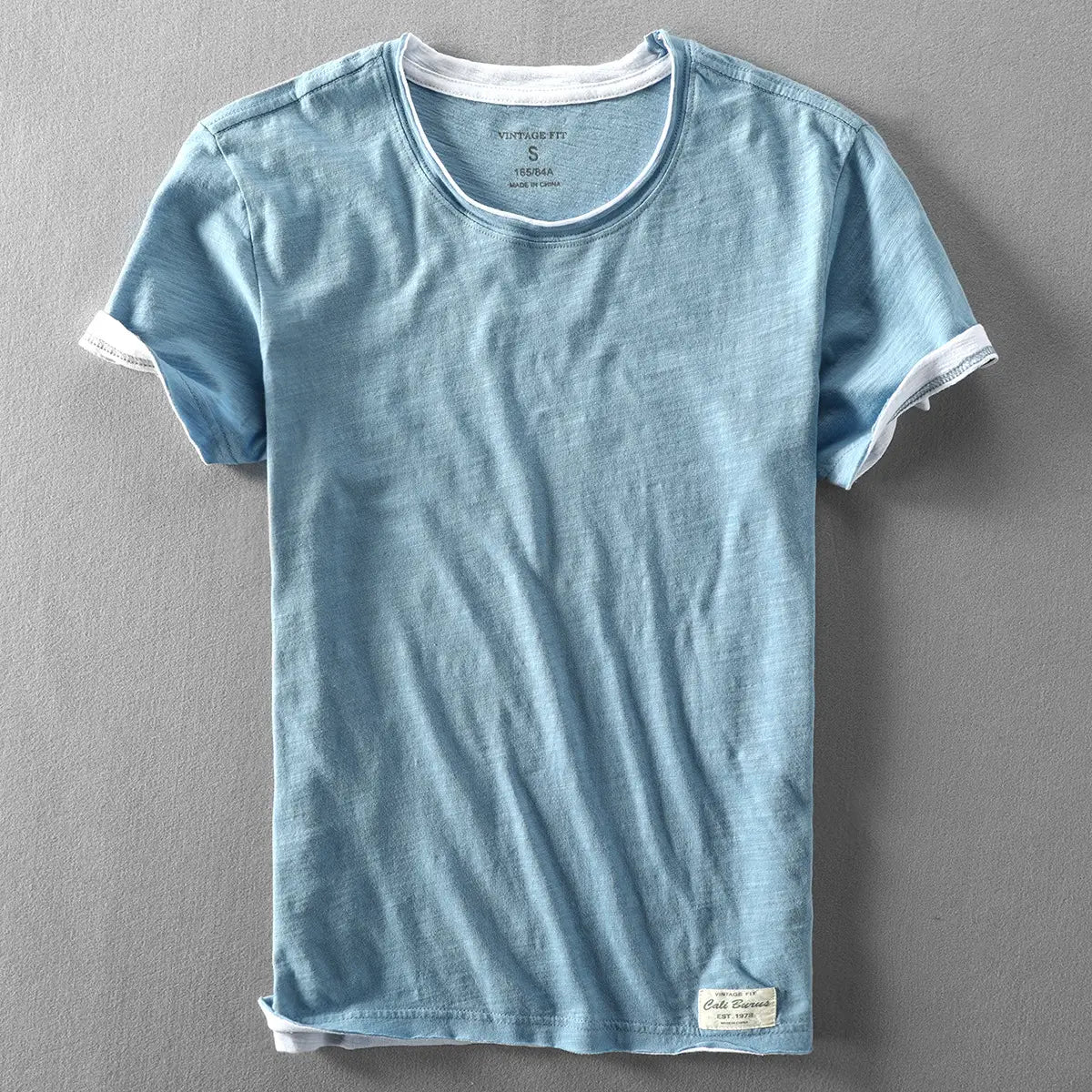 Hellblaues Baumwoll-T-Shirt für Herren mit Kontrastbesatz und weißem Besatz am Kragen sowie an den Ärmelsäumen als Sommeroberteil für den Freizeitbereich.