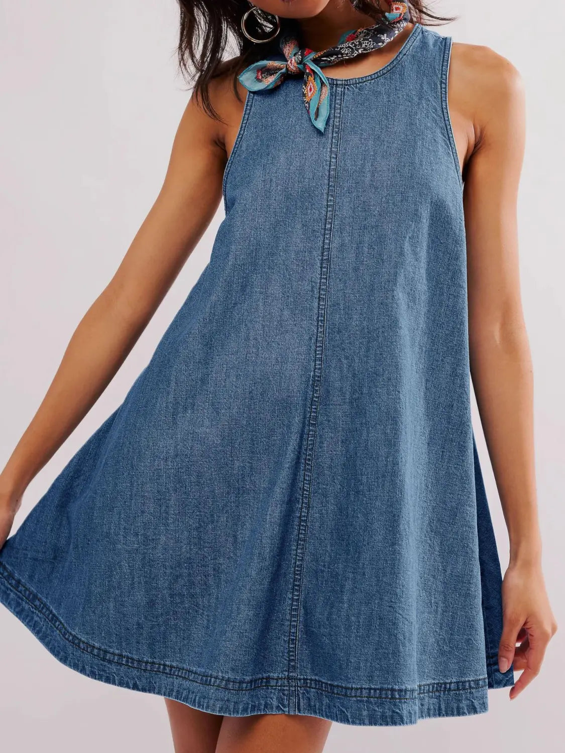 Ein ärmelloses Jeans-Minikleid in mittlerer Blau-Waschung mit rundem Halsausschnitt und einem gemusterten Tuch, das vorne zu einer Schleife gebunden ist, einschließlich eines hinten offenen Schleifen-Details.