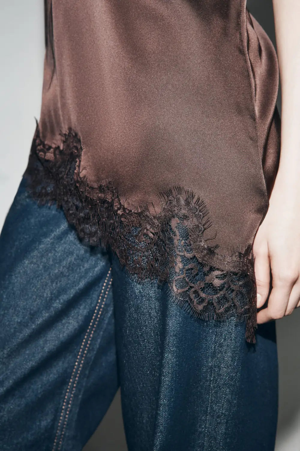 Ein braunes Satin-Camisole-Top mit zartem schwarzem Spitzenbesatz entlang des Saums.