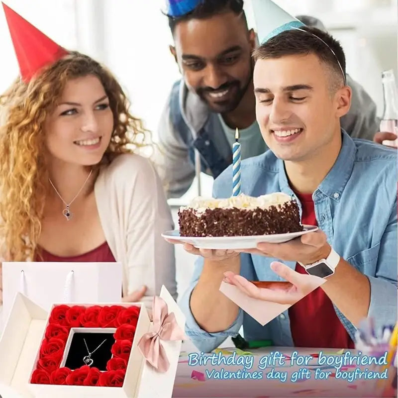 A heart-shaped silver pendant necklace with projection feature nestled in a black velvet box surrounded by vibrant red roses in the projection heart necklace and rose gift box set.