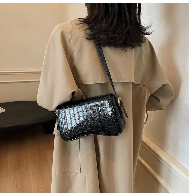 Black crocodile-embossed leather messenger bag with gold-tone hardware designed as a minimalist crossbody organ bag.