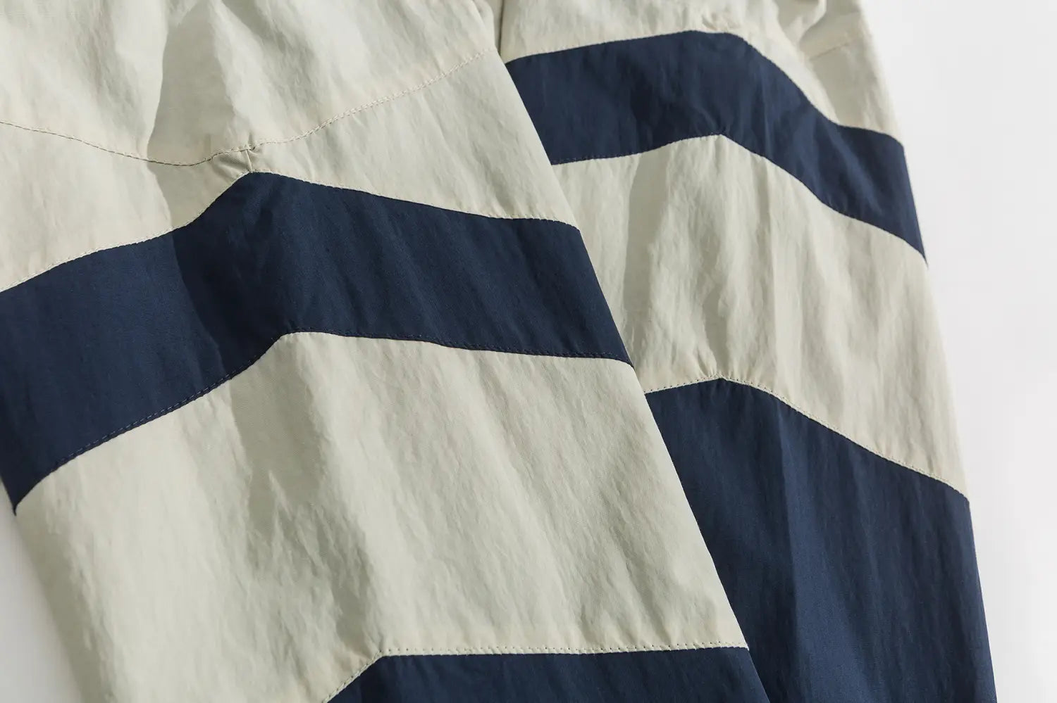 Short à rayures horizontales crème et bleu marine, en tissu léger légèrement froissé, assorti à une veste coupe-vent ample à blocs de couleurs brodés.