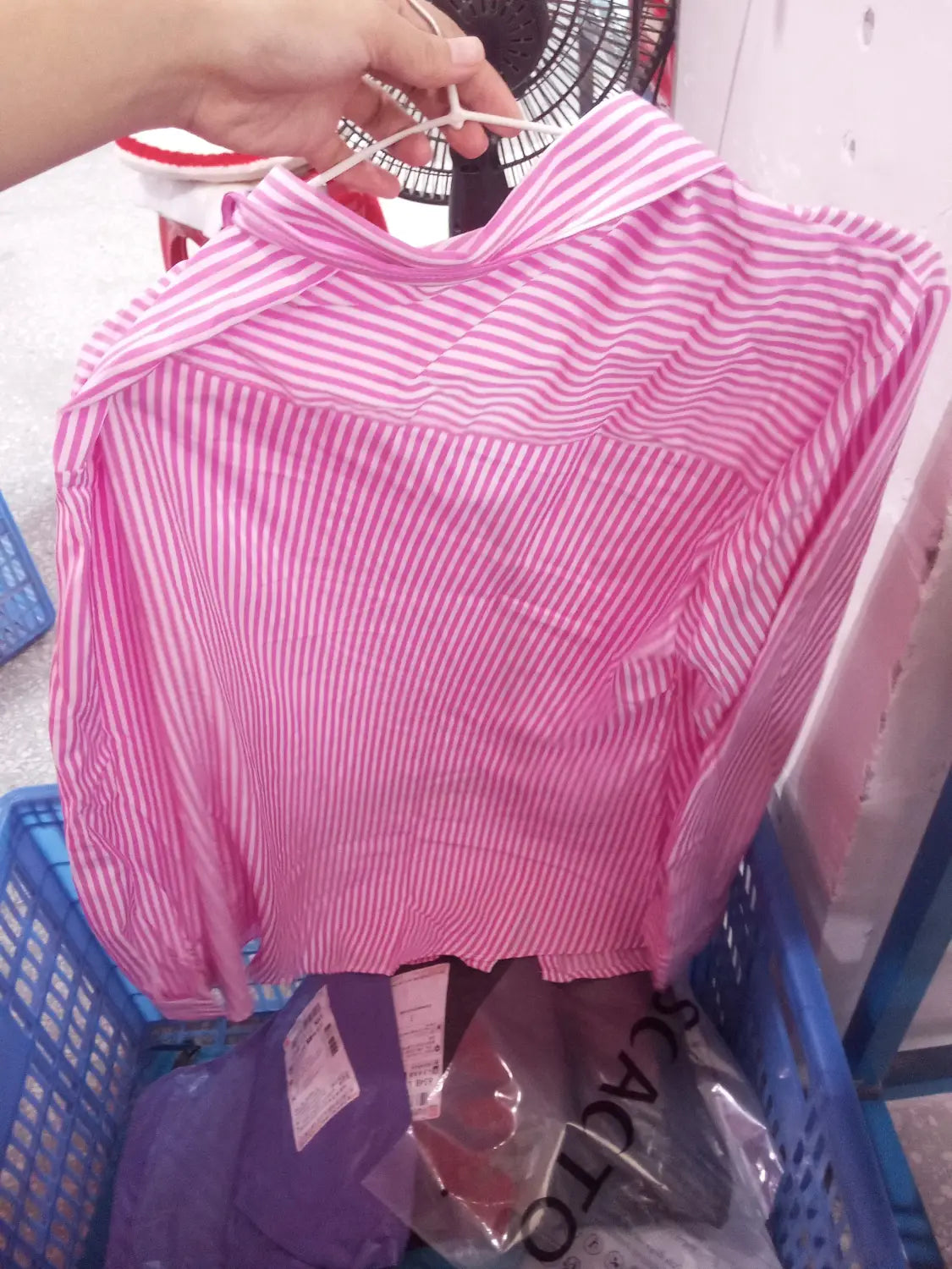 Chemise boutonnée à manches longues à rayures verticales rose et blanche avec col, présentée sur un cintre, adaptée à un usage décontracté.