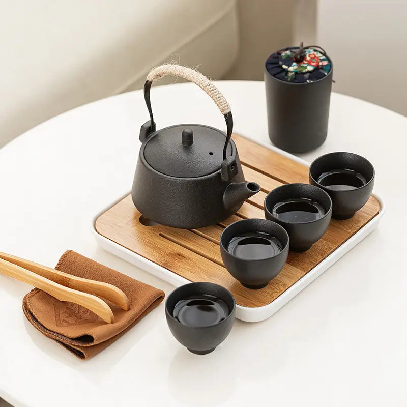 Black cast iron teapot with textured rope-wrapped handle and matching lid from ceramic travel tea set with bamboo tray and case.
