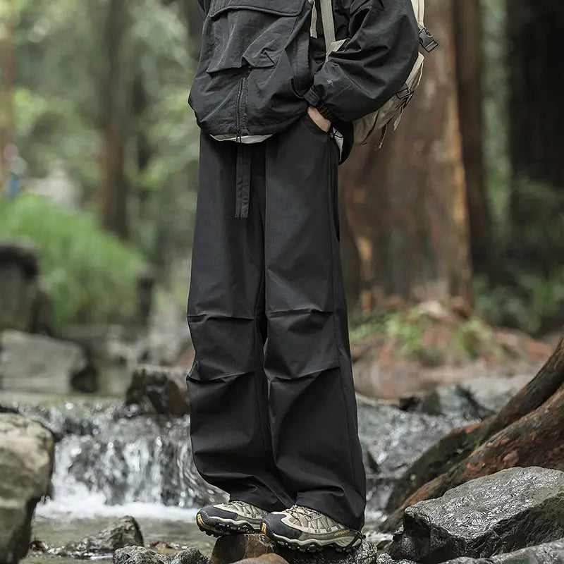 Black pleated cargo hiking pants for men and women featuring multiple utility pockets and a drawstring waistband.