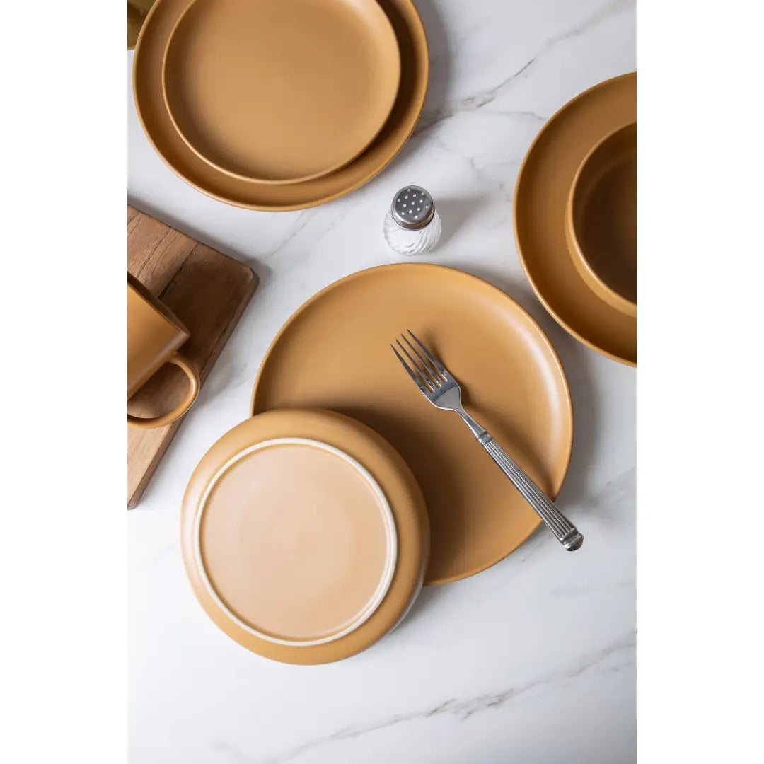 Set of 12 piece matte tan ceramic stoneware dinnerware plates with subtle white rim accents designed for four people.