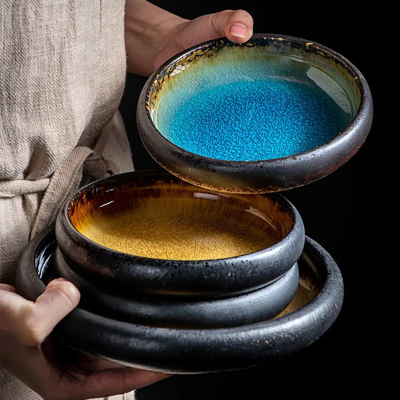 Handcrafted ceramic bowl kiln glazed bone china round plate with a glossy crackled glaze in vibrant blue and gold hues and dark earthy exterior.