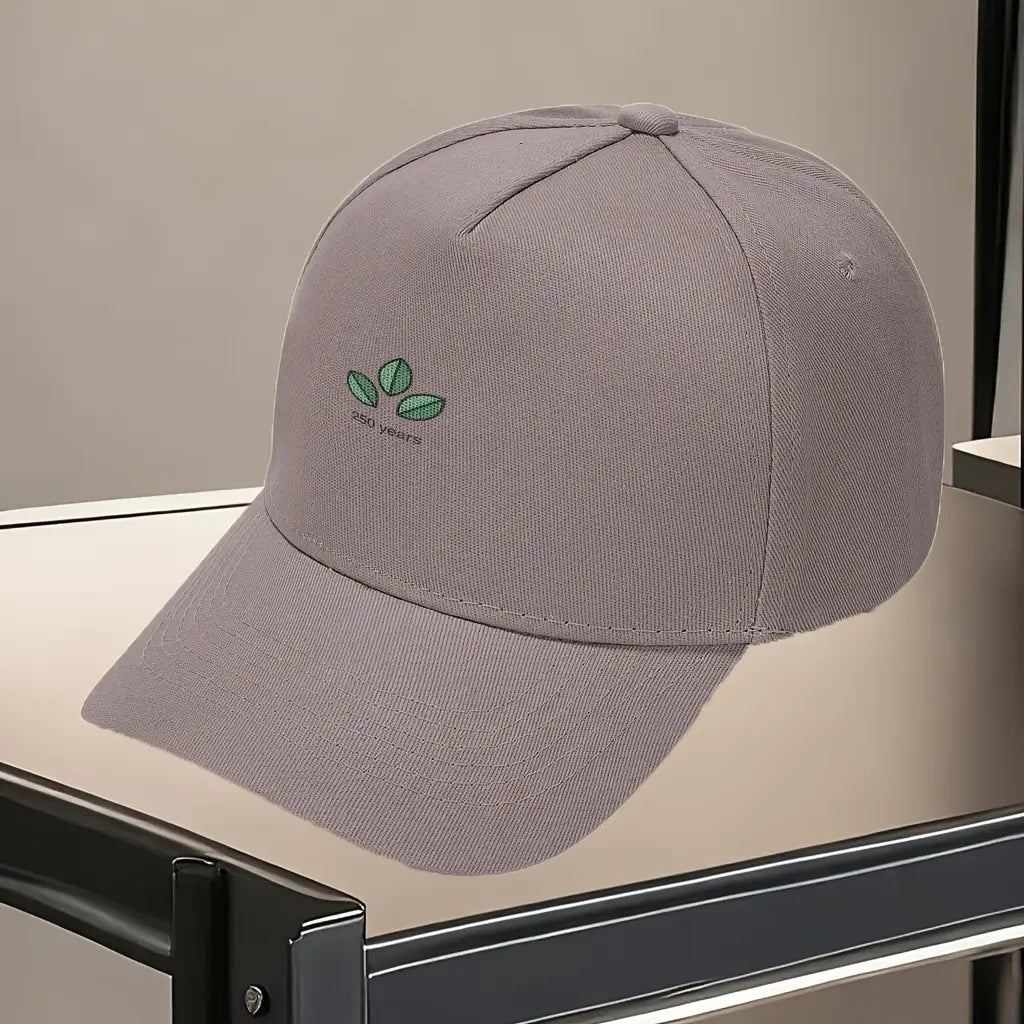 A soft gray baseball cap made of fabric featuring a subtle embroidered logo of three green leaves with 250 years written beneath for the Usa 250th anniversary celebration.