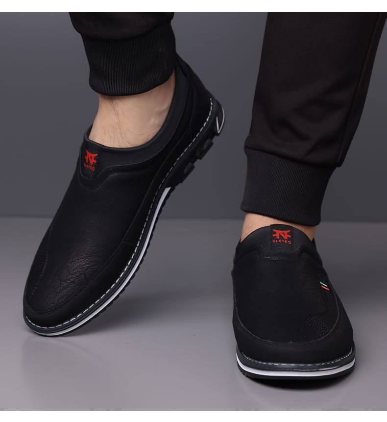 Mocasines de vestir de cuero para hombre, estilo casual de negocios, en negro con parte superior texturizada, costura blanca a lo largo del borde de la suela y logotipo rojo en el tacón visto desde la parte trasera
