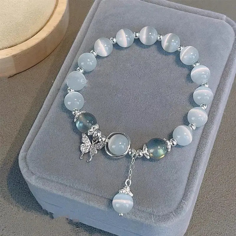 A delicate crystal butterfly cat’s eye bead bracelet featuring light blue cat’s eye beads and silver-toned metal accents including a butterfly charm and a dangling bead.