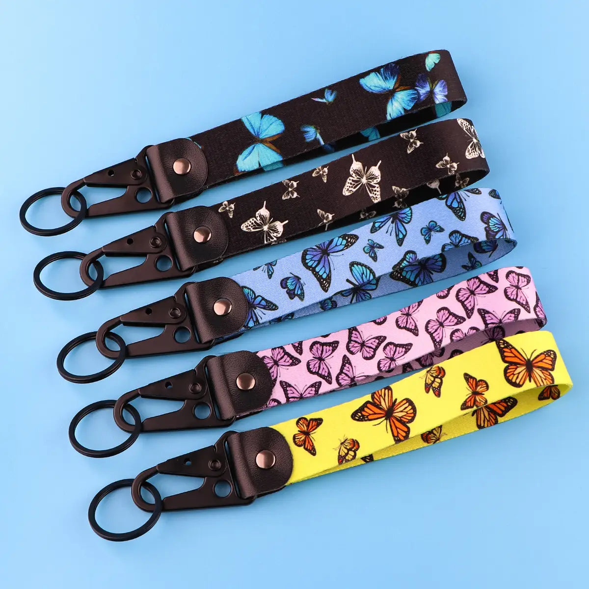 five butterfly wrist strap keychains with metal clip featuring butterfly patterns in assorted colors including black blue pink and yellow designed for holding keys securely