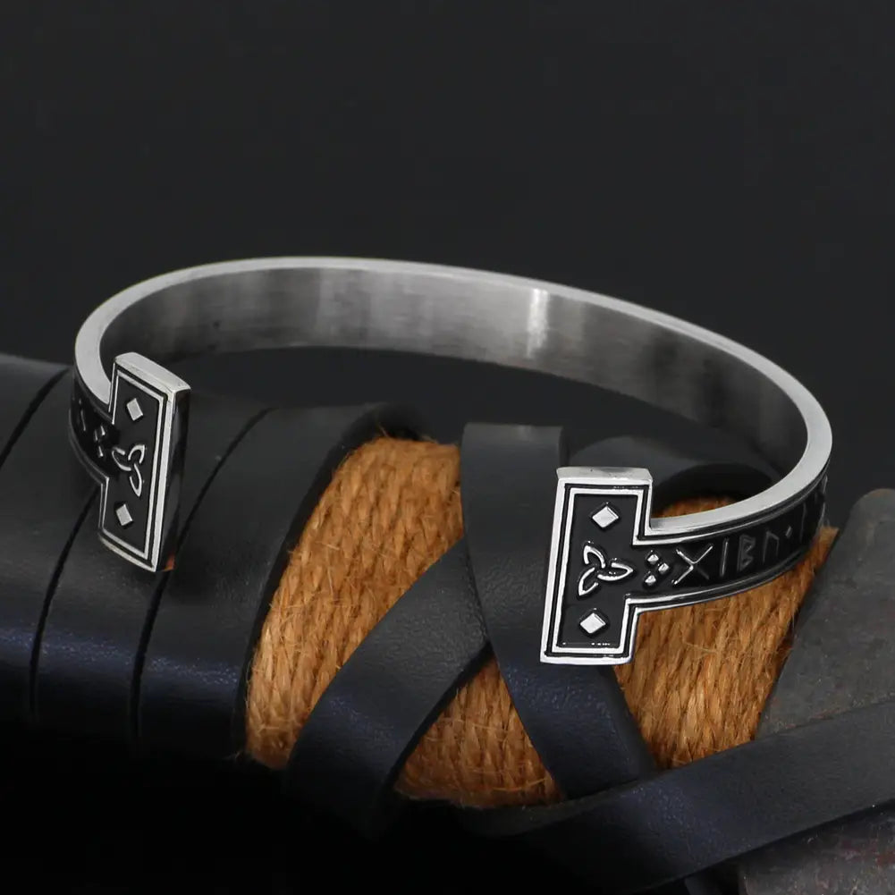 adjustable viking rune titanium steel open cuff bracelet featuring a silver-toned metal with intricate norse-inspired engravings and a black leather strap wrapped around its center.