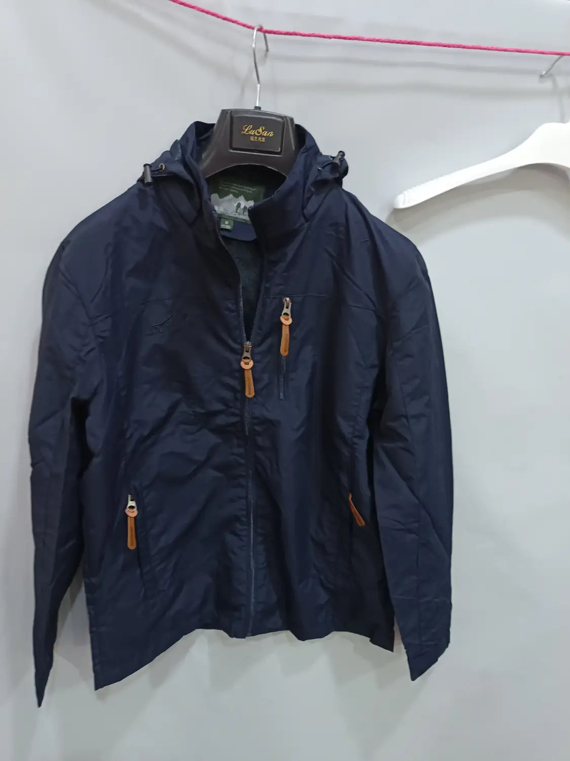 Chaqueta de senderismo con capucha impermeable color azul marino, con tiradores de cremallera de cuero color camel, diseñada para actividades al aire libre.