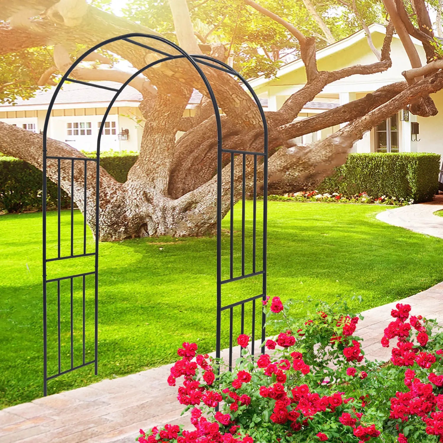 Black metal garden arch with arched top and vertical slats made of wrought iron set against green grass and blooming red roses.