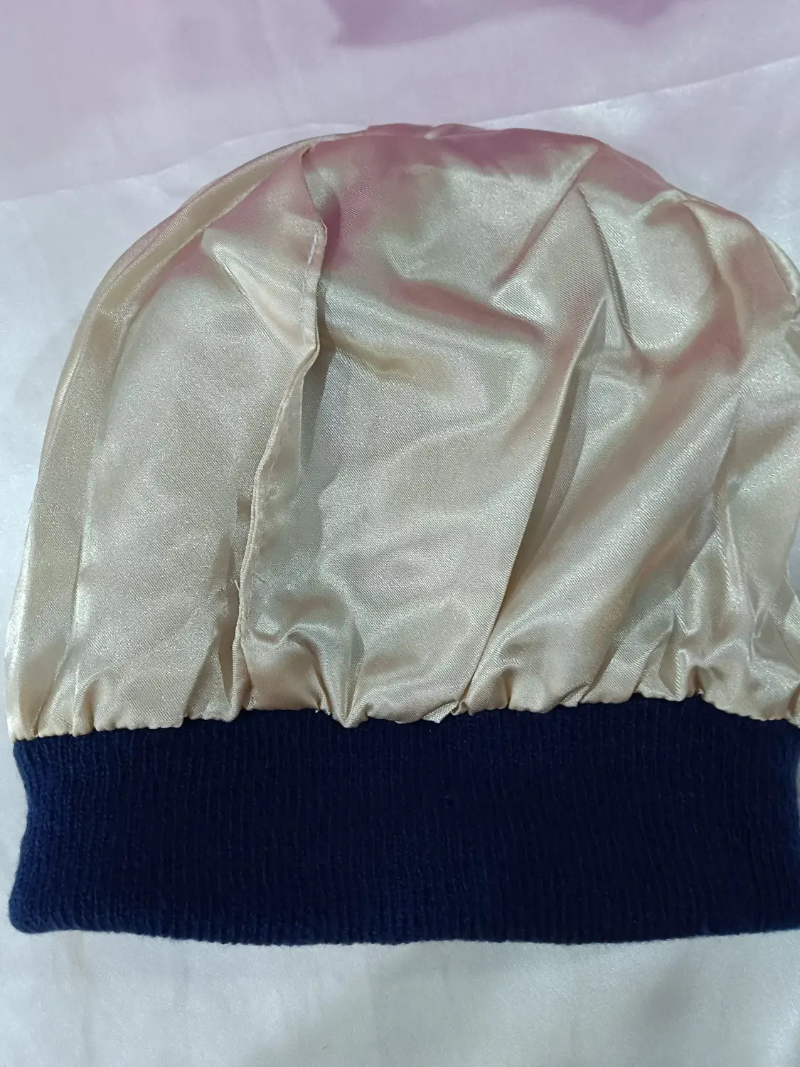 Satin lined knit beanie warm winter hat featuring a shiny satin-like gold bonnet with a ribbed navy blue knit band at the bottom.