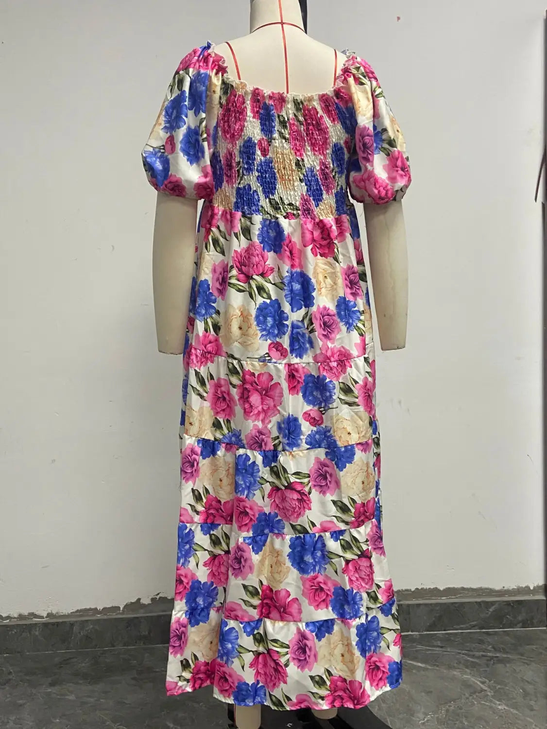 A vibrant floral print smocked tiered midi dress with puffy short sleeves and a square neckline featuring bold pink blue and cream blossoms on white satin-like fabric.