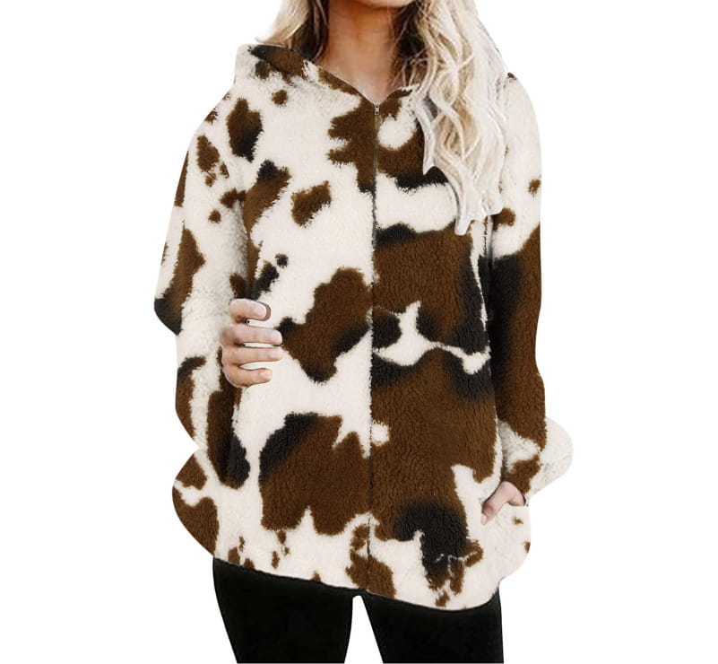 Una chaqueta acolchada tipo zip-up de vellón con capucha, marrón y blanca con estampado de vaca, cierre frontal con cremallera y mangas largas.