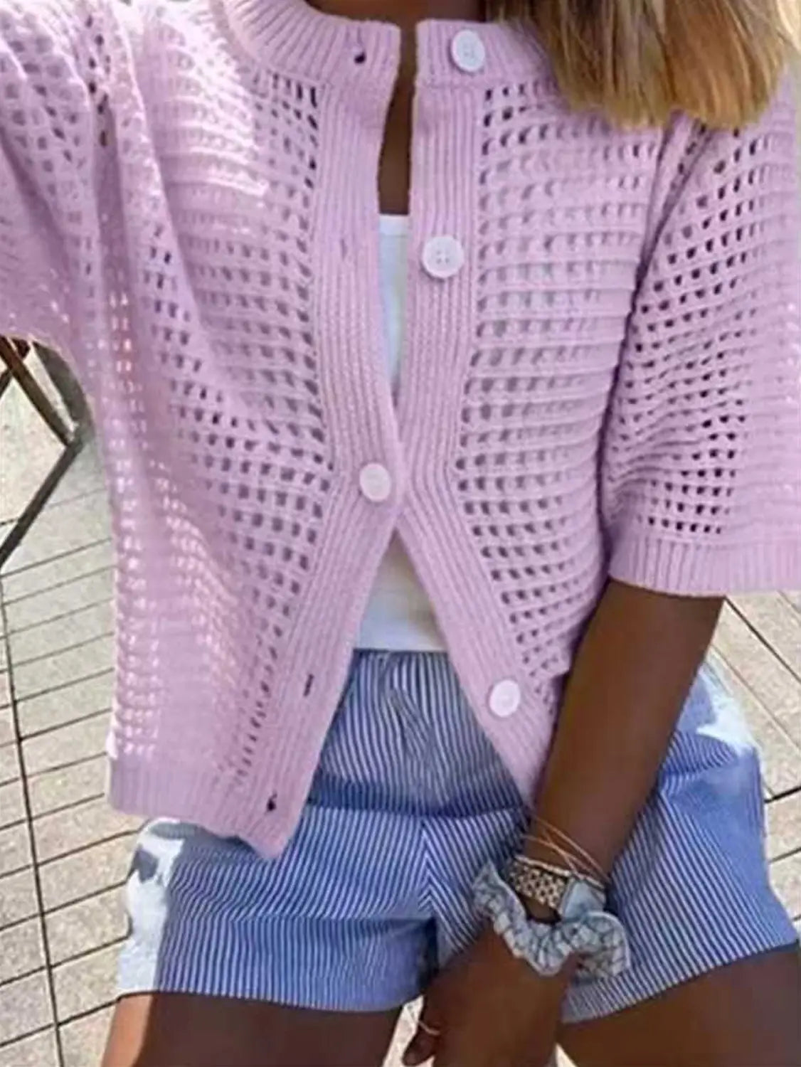 Un delicado suéter tipo cárdigan de punto rosa claro con patrón de calado tipo encaje, mangas de manga corta y botones blancos a juego.