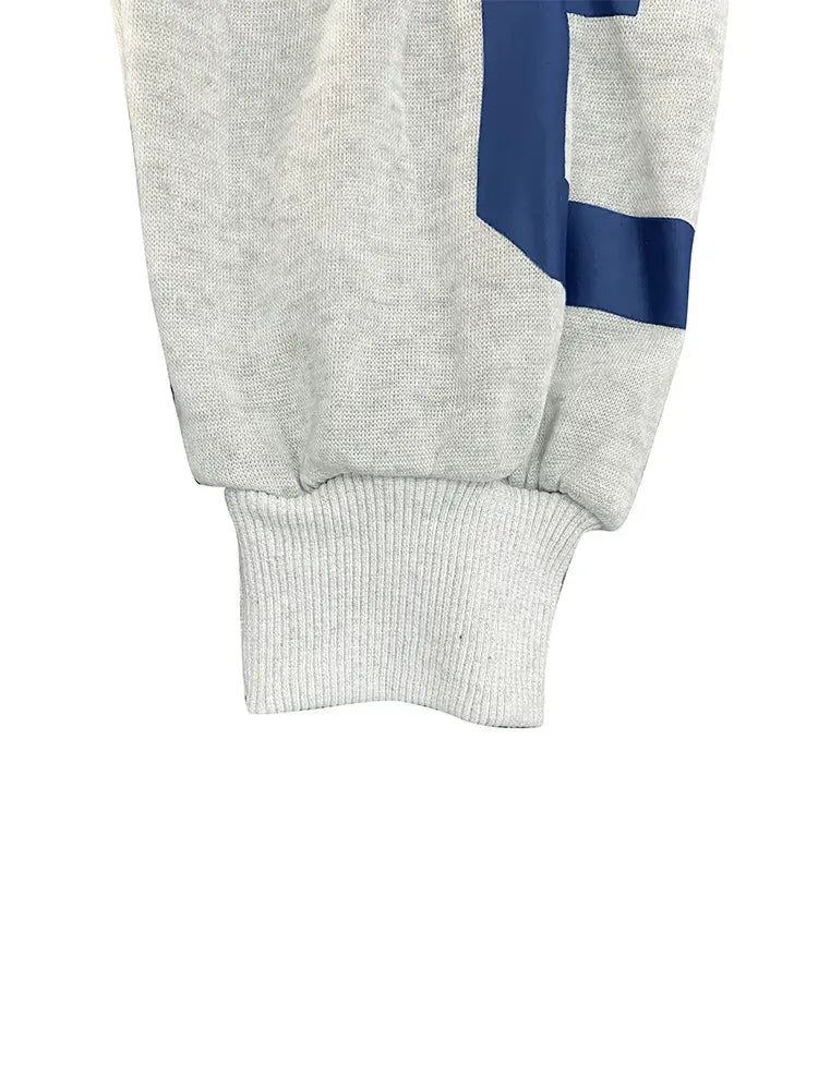 Poignet de survêtement chiné gris avec finition en maille côtelée et motif de rayure géométrique bleue audacieuse, associé à un sweat-shirt à capuche zippé imprimé graphique.