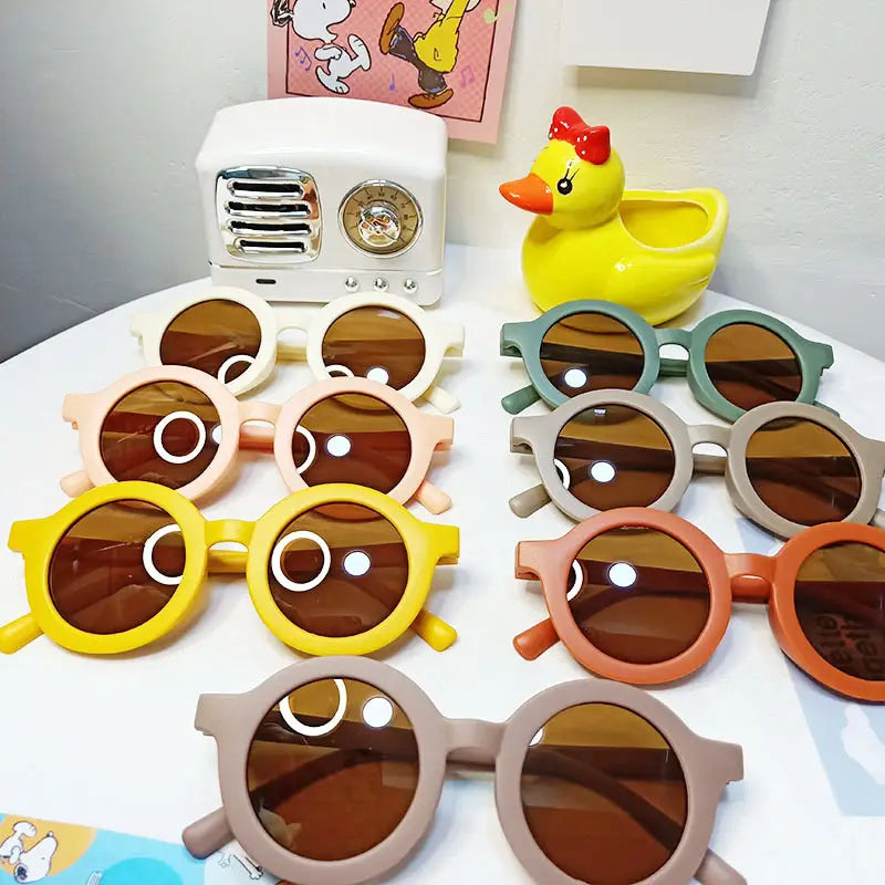 Un ensemble de lunettes de soleil pour chiens rétro rondes et colorées avec des montures orange, des verres marron et des accents circulaires blancs ludiques sur les montures, destinées aux enfants.