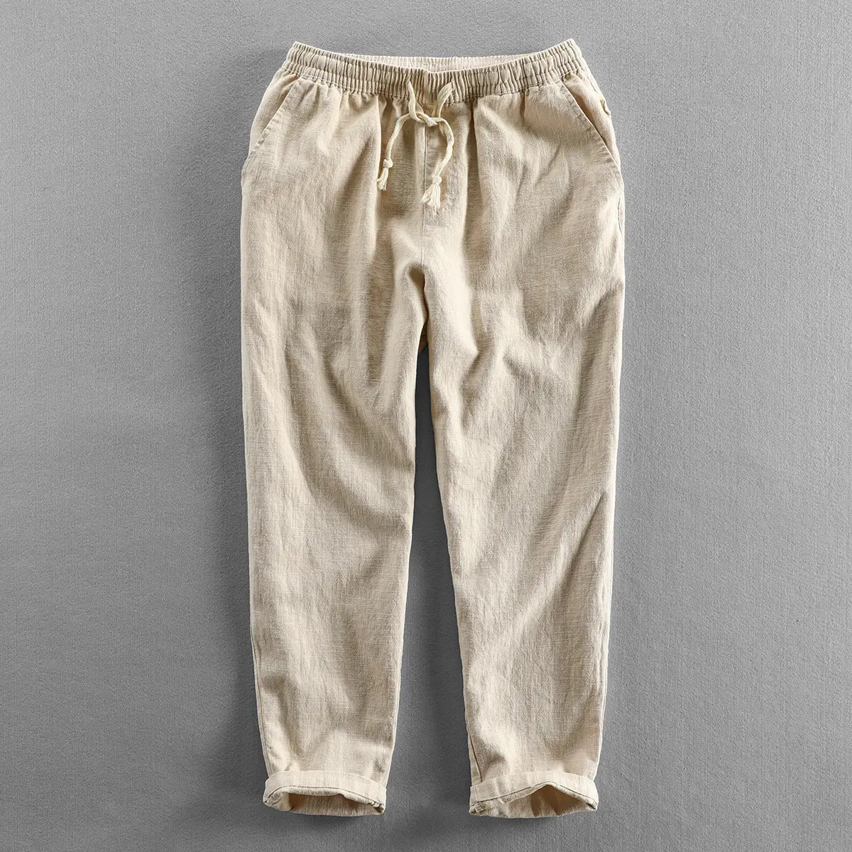 Beige linen trousers with an elastic waistband and drawstring featuring a relaxed fit and rolled cuffs in men’s relaxed fit drawstring linen joggers.