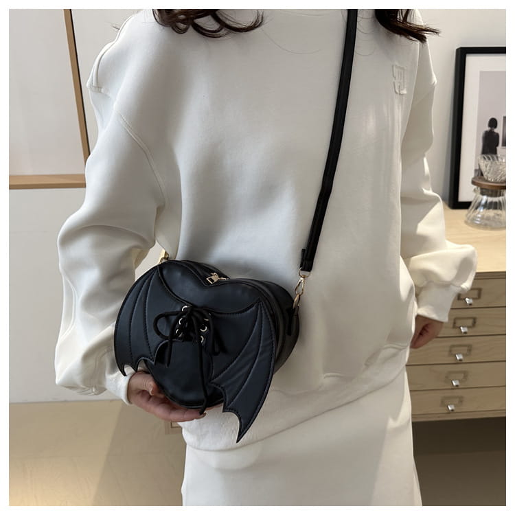 Black bat wing heart crossbody bag with lace up detail made of textured leather-like material.