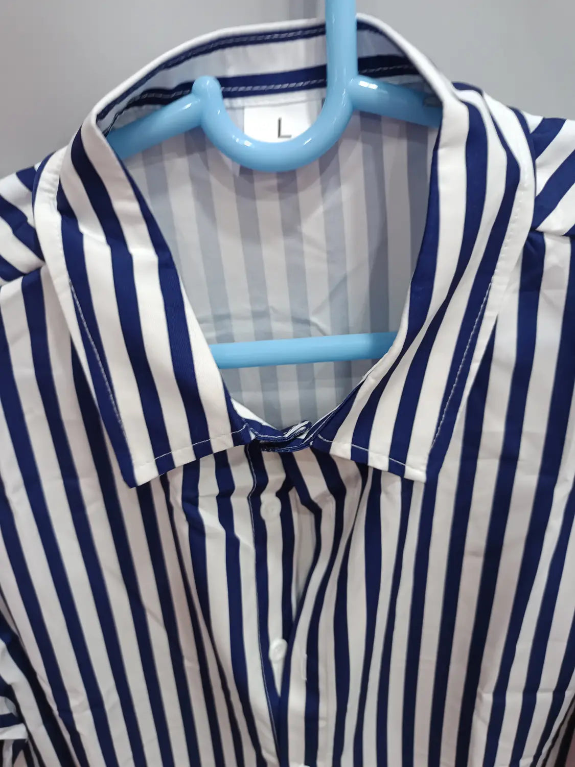 Chemise décontractée à manches longues rayée verticalement bleu et blanc pour hommes, avec col suspendu sur un cintre en plastique bleu clair.
