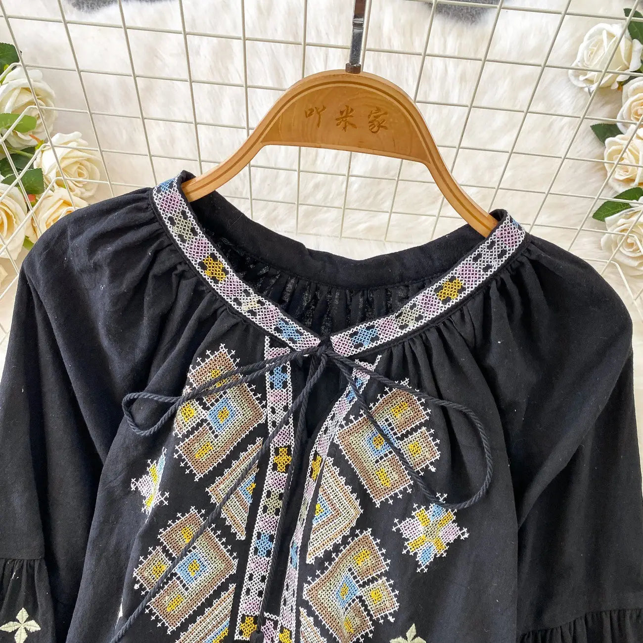 Black embroidered lantern sleeve tie neck blouse with intricate geometric embroidery in beige yellow and blue tones across the chest and neckline.