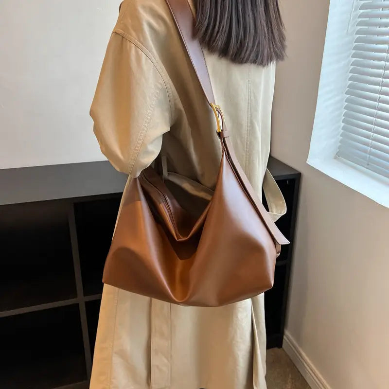 A sleek caramel-colored leather shoulder bag with gold buckle and strap features a minimalist design and gold-tone hardware.