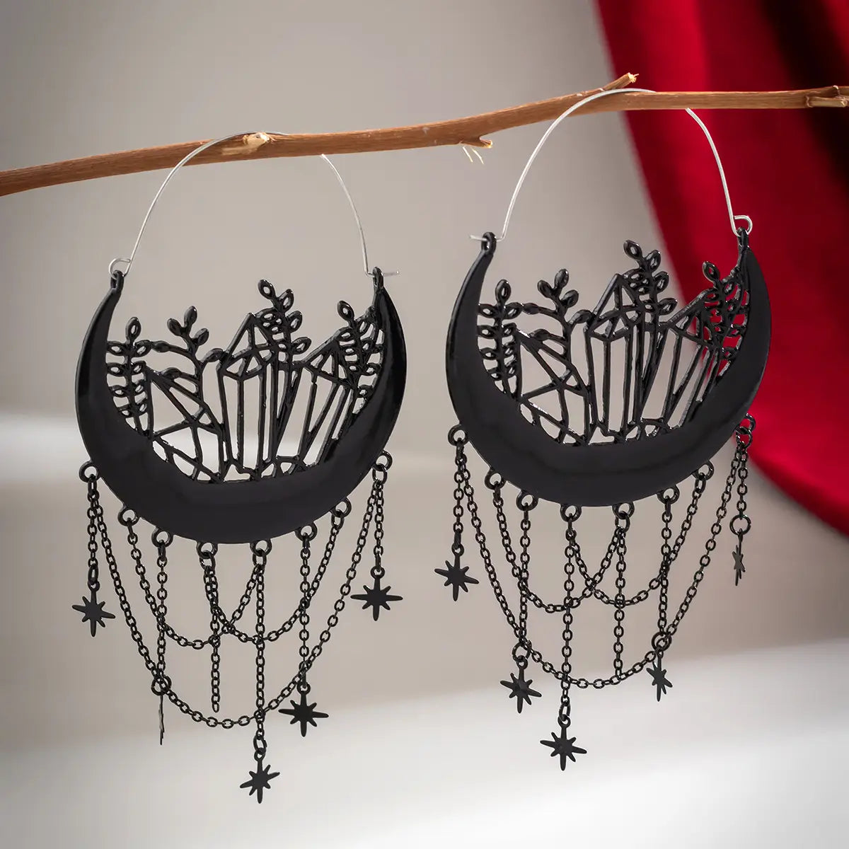 Ohrringe mit schwarzem Halbmond-Tassel-Design mit aufwendig gestalteten Kristall- und Pflanzendekoren im Cut-out-Stil, mit baumelnden Ketten, die mit Stern-Anhängern verziert sind.