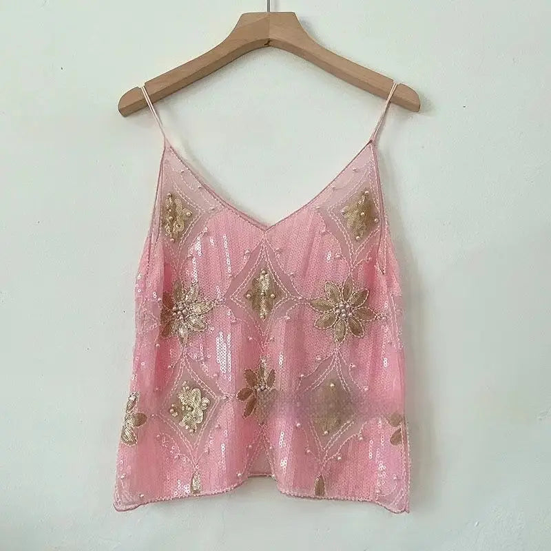 Ein zartes, rosafarbenes Pailletten-gesticktes Mesh-Camisole-Top mit goldfarbener Blumeneinstickerei und perlenbesetzten Details, hängend an einem Holzkleiderbügel.