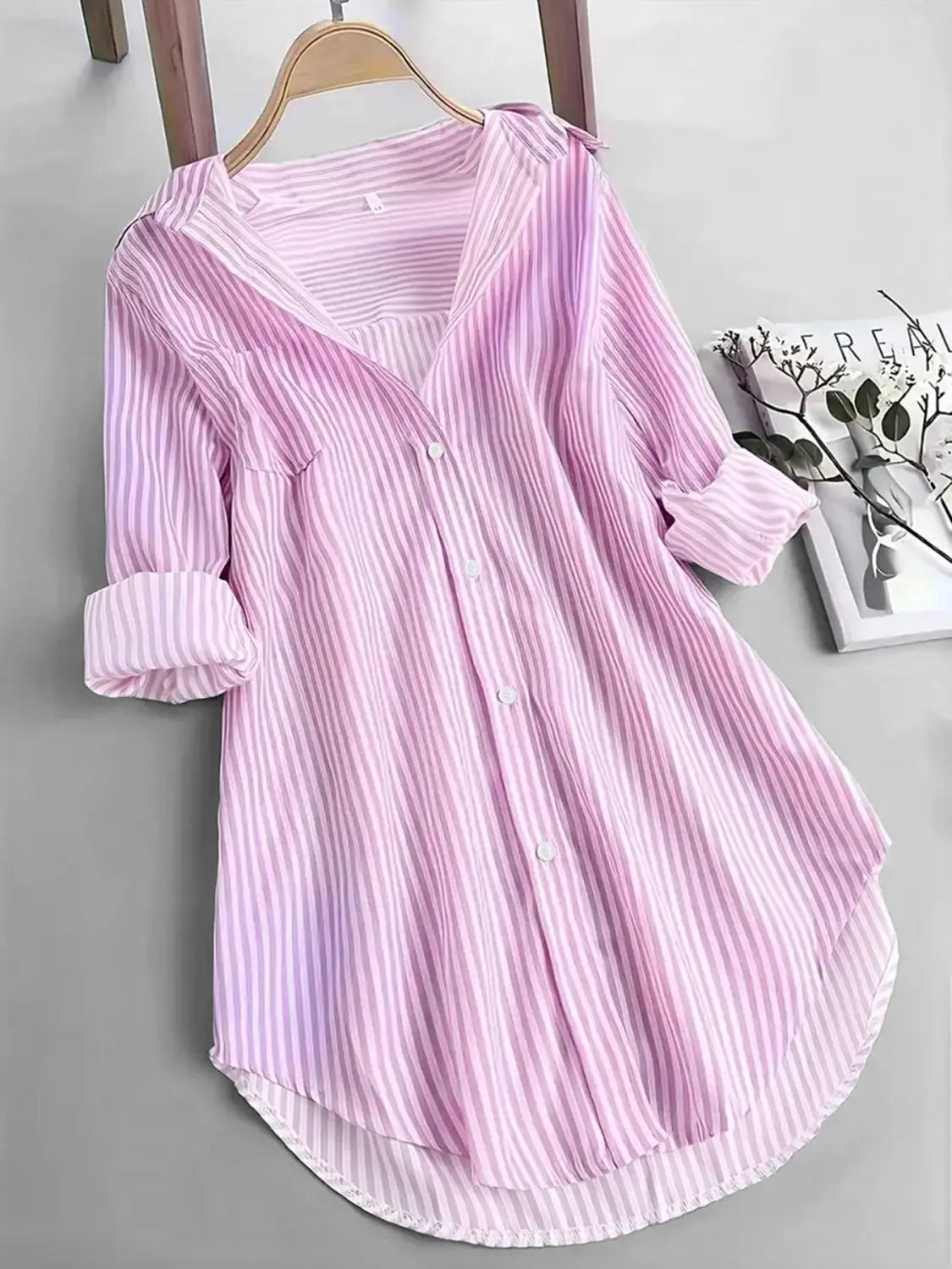 Chemise boutonnée décontractée à manches longues à rayures verticales rose tendre et blanches, manches retroussées, suspendue à un cintre en bois.