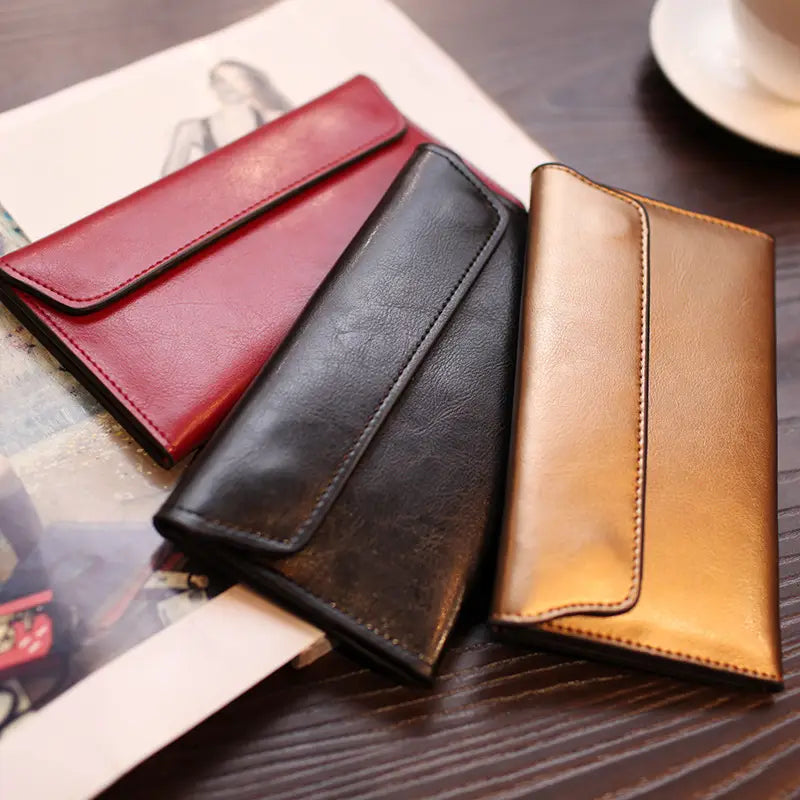 Three slim retro cowhide leather flap wallets in red black and gold tones with contrast stitching and stitched edges.