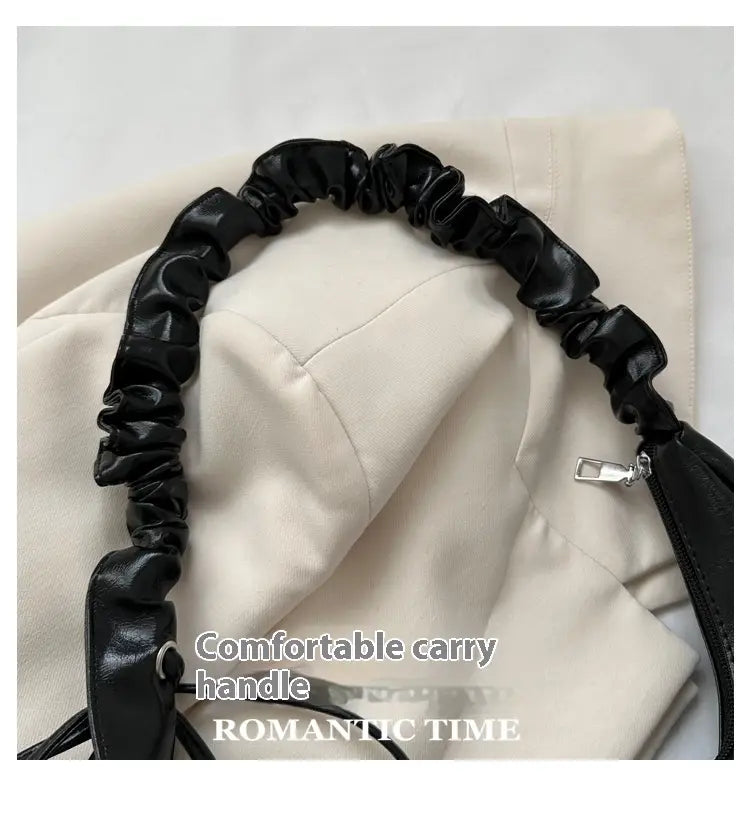 Black ruched faux leather shoulder strap with a silver zipper pull on a patent leather ruched shoulder bag handbag.