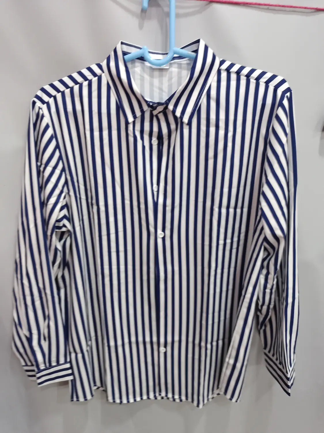 Chemise décontractée à manches longues rayée verticalement bleu marine et blanc pour hommes, suspendue sur un cintre bleu.