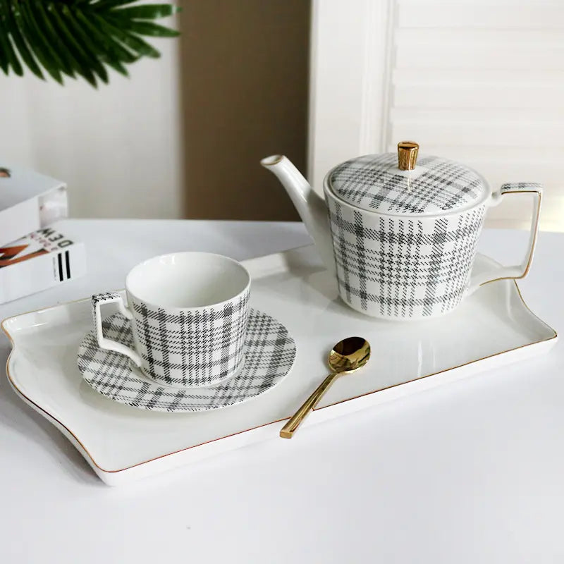 White ceramic teapot with black and gray plaid pattern and gold-trimmed lid knob and handle from ceramic tea set with plaid teapot and gold trim tray.