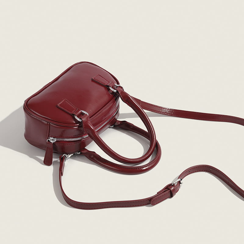 A glossy burgundy pu leather small square handbag with a structured rectangular shape, dual top handles, and an adjustable shoulder strap.