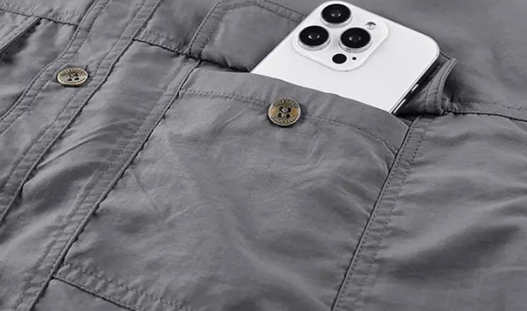 A white iPhone with a triple-lens camera system rests partially in the pocket of a gray textured fabric men solid workwear shirt short sleeve.