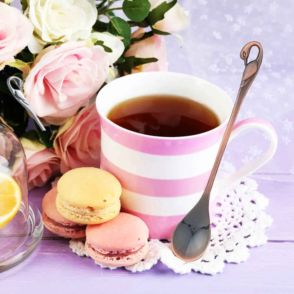 Une tasse en céramique à rayures rose et blanc, remplie de thé foncé, accompagnée d’une cuillère à dessert dorée du Coffret de coutellerie Swan Cutlery Set en cuillères et fourchettes à dessert dorées.