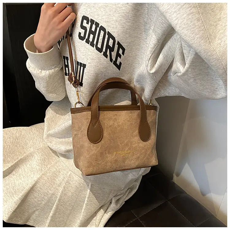 Beige canvas retro bucket bag mini tote with brown leather handles and trim designed as a textured canvas shoulder handbag.