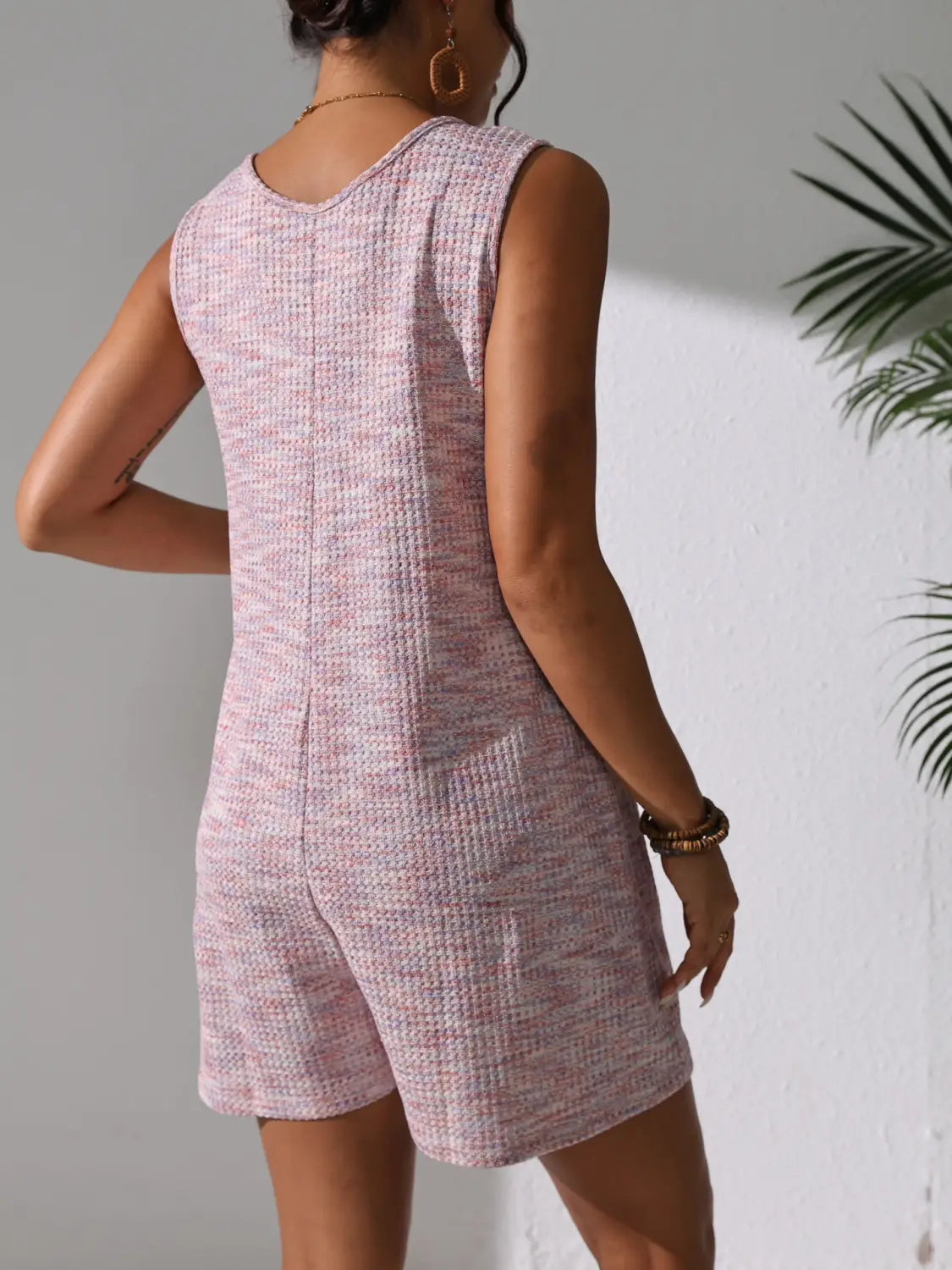 A sleeveless light pink waffle knit button front romper with a textured pattern and rounded neckline.
